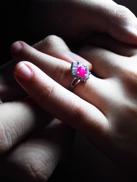 A boyfriend placing a light rose colored Amethyst on his girlfriend's ring finger at a proposal.
