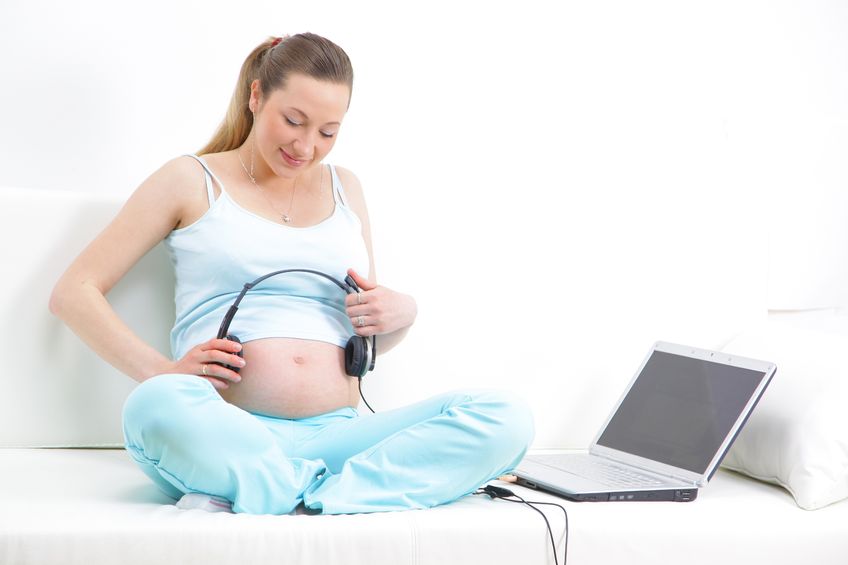 a beautiful pregnant woman holding the headset to her tummy so her the child from the womb can hear music