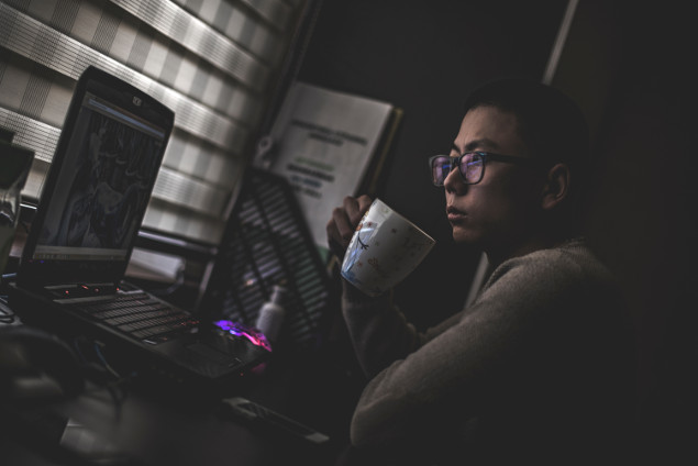 a young guy taking a cup of coffee in front of his computer